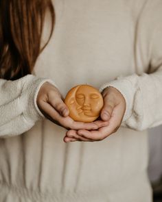 a woman holding a cookie in her hands with a face on it's side