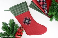 three christmas stockings with plaid designs on them next to evergreen branches and potted plants