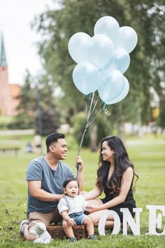 a man, woman and child sitting in the grass with balloons