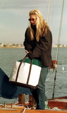 a woman sitting on the back of a boat holding a large white and green tote bag