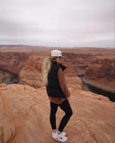 a woman standing on the edge of a cliff looking out at canyons and cliffs