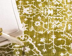 a green and white rug with gold trimmings on the edge, next to a pair of scissors