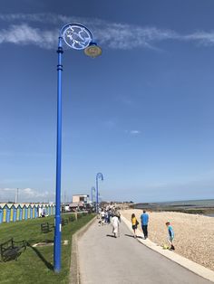 several people walking on the sidewalk next to a blue street light