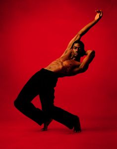 a man in black pants and no shirt is doing a dance move against a red background