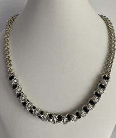 This chainmaille necklace measures 18 inches in length and is a combination of two weaves-open round for the chain and Jacob's Ladder for the focal. Tiny sterling silver rings make up the open round chain which is tubular in form. The focal weave is Jacob's Ladder, a variation of open round that has rings captured within. The medium size sterling rings capture black and frost gray anodized aluminum rings.  The clasp is a 1/4 inch sterling lobster claw.  A truly unique necklace to wear. Jump Ring Chain Link Jewelry For Jewelry Making, Elegant Black Chainmail Jewelry, Silver Jewelry With Box Chain And Round Beads, Elegant Sterling Silver Chainmail Necklace, Silver Rolo Chain For Jewelry Making, Black Sterling Silver Link Necklace, Silver Necklace With Box Chain And Round Beads, Silver Jewelry With Rolo Chain For Jewelry Making, Elegant Silver Wire Wrapped Chain Necklace