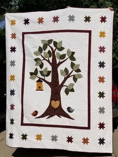 a white quilt with a tree and birdhouse on it in front of a parked car