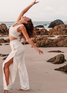 a woman standing on top of a sandy beach next to the ocean with her arms in the air