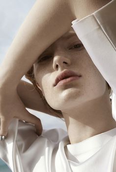 a close up of a person wearing a white shirt and holding their hands on his head