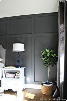 a white bed sitting in a bedroom next to a lamp on a table with a potted plant