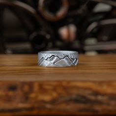 a silver ring with mountains on it sitting on top of a wooden table