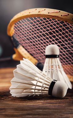 two badminton racquets and three white shuttles on a wooden table top