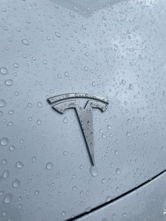 the tesla logo is on top of a car in the rain covered parking lot with water droplets