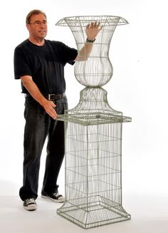 a man standing next to a tall metal birdcage with his hands on it