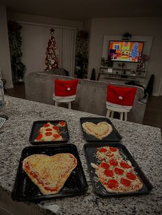 three heart shaped pizzas sitting on top of trays in front of a tv