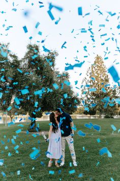 a man and woman kissing under blue confetti on top of a grass covered field