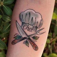 a chef's hat and knife tattoo on the left arm, with green leaves in the background