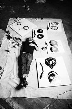 a man laying on top of a sheet of paper next to various art pieces and scissors