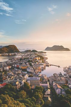 an aerial view of a city on the water with mountains in the background at sunset