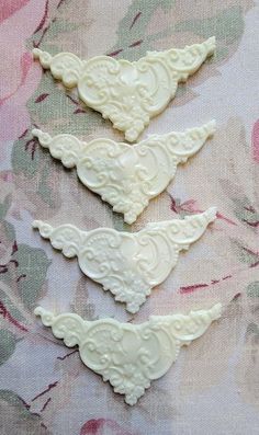 three pieces of white lace sitting on top of a flowery cloth covered tablecloth