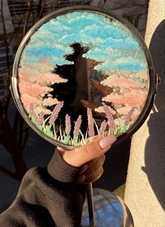 a person holding up a mirror with trees and grass on the outside, in front of a building