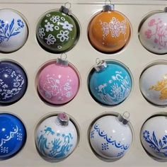 twelve different colored ornaments are in a display case with white and blue designs on them