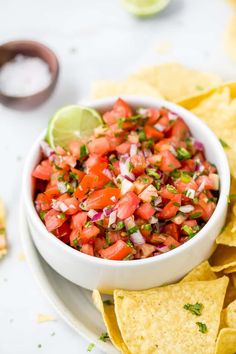 a white bowl filled with salsa surrounded by tortilla chips and lime wedges