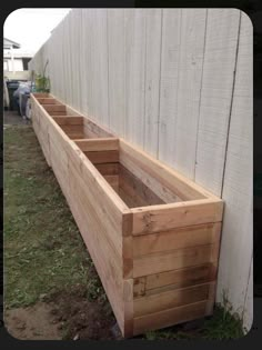 a wooden planter sitting on the side of a white wall next to a grass covered yard