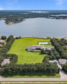 an aerial view of a large green field next to a body of water with houses in the background