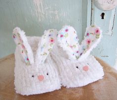 two white crocheted bunny slippers sitting on top of a wooden table next to a blue door