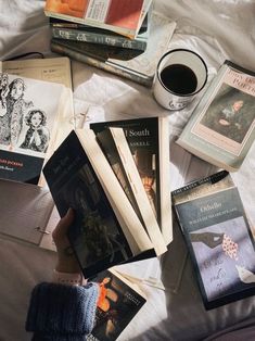 a bed topped with lots of books next to a cup of coffee