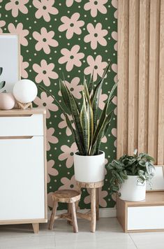 a living room with green and pink wallpaper, potted plants and wooden stools