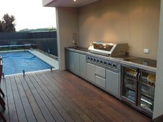 an outdoor kitchen with stainless steel appliances and wood flooring, overlooking a swimming pool