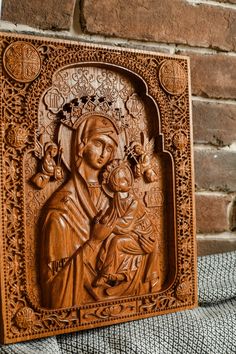 an intricate carved wooden icon depicting the virgin mary and child jesus on a brick wall