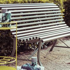 a wooden bench sitting next to bushes and a yellow trash can in front of it