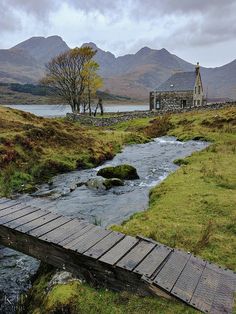 a small wooden bridge over a stream in the middle of a grassy field with mountains in the background