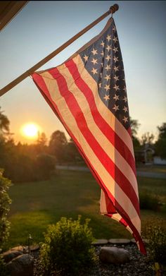 an american flag hanging from a pole in front of the sun setting over a field