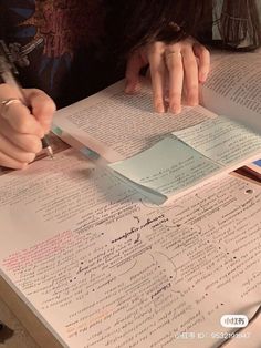 a person writing on top of a book with a pen and paper clippings