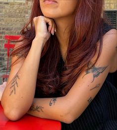 a woman sitting at a red table with tattoos on her arm and shoulder, looking off to the side