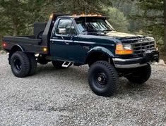 a blue pick up truck parked on top of a gravel covered parking lot next to trees