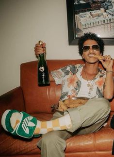 a man sitting on top of a brown couch holding a bottle of beer and food