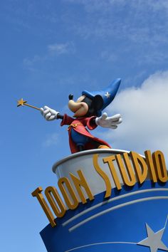 a statue of mickey mouse on top of the disney studio sign in front of a blue sky