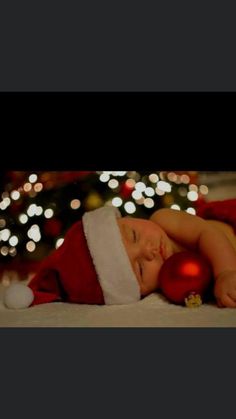 a baby wearing a santa hat sleeping next to a christmas tree