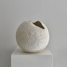 a large white vase sitting on top of a white pedestal in front of a gray wall