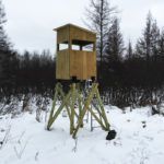 there is a small wooden tower in the middle of the snow covered field with trees behind it