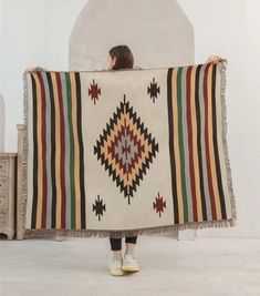 a woman holding up a blanket in front of a white wall