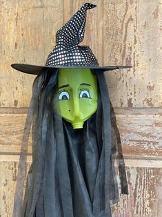 a green mask with black hair and a hat on it's head, sitting against a wooden door