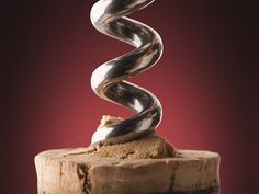 a silver spiral sculpture on top of a piece of wood in front of a red background