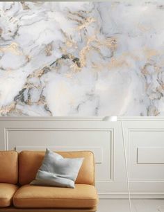 a couch sitting in front of a wall covered in white and gold marbled paper