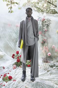 a man in a suit and tie standing on a bed of flowers with a yellow bag