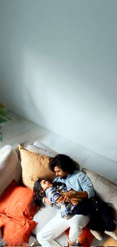 a man and woman cuddle together on a couch with orange pillows in the background